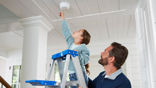 daughter on ladder testing alarm with father